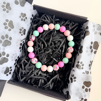 Silicone beaded dog necklace made with 15mm round beads in pink, green, white and a floral flowers print. On a strong, elastic stretch cord. Pictured inside the gift box.￼