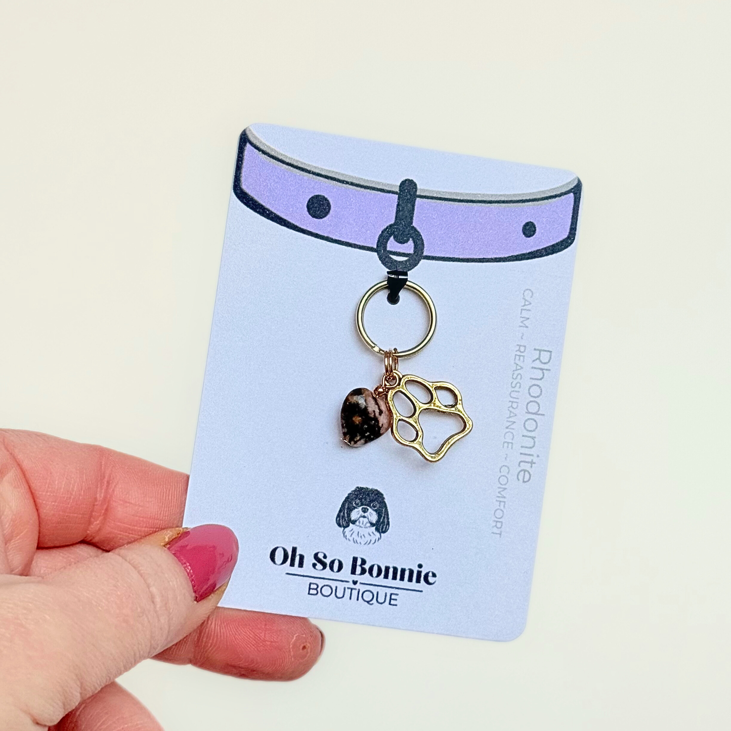 Crystal for dogs pet collar charm featuring a 10mm rhodonite heart shaped bead and a brass gold coloured paw print tag. Pictured on the display card.￼