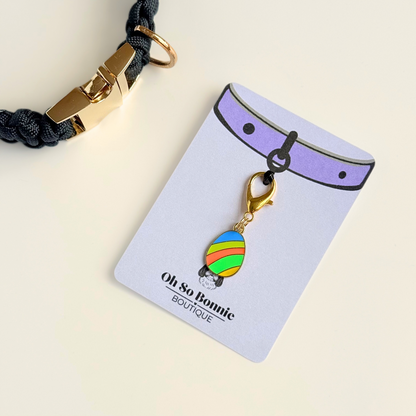 Colourful striped Easter egg enamel dog collar charm that easily attaches to collars and harnesses with a gold plated lobster clasp. Pictured on the display card next to a black paracord dog collar.￼