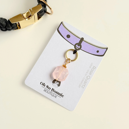Handmade dog collar charm featuring a 17mm pink rose quartz natural gemstone faceted square crystal bead. Hung on a gold plated brass split ring with a daisy gold spacer bead that attaches onto your pet collar. Rose quartz can help pets with love, comfort and calming. Pictured on the display card, next to a black paracord dog collar.