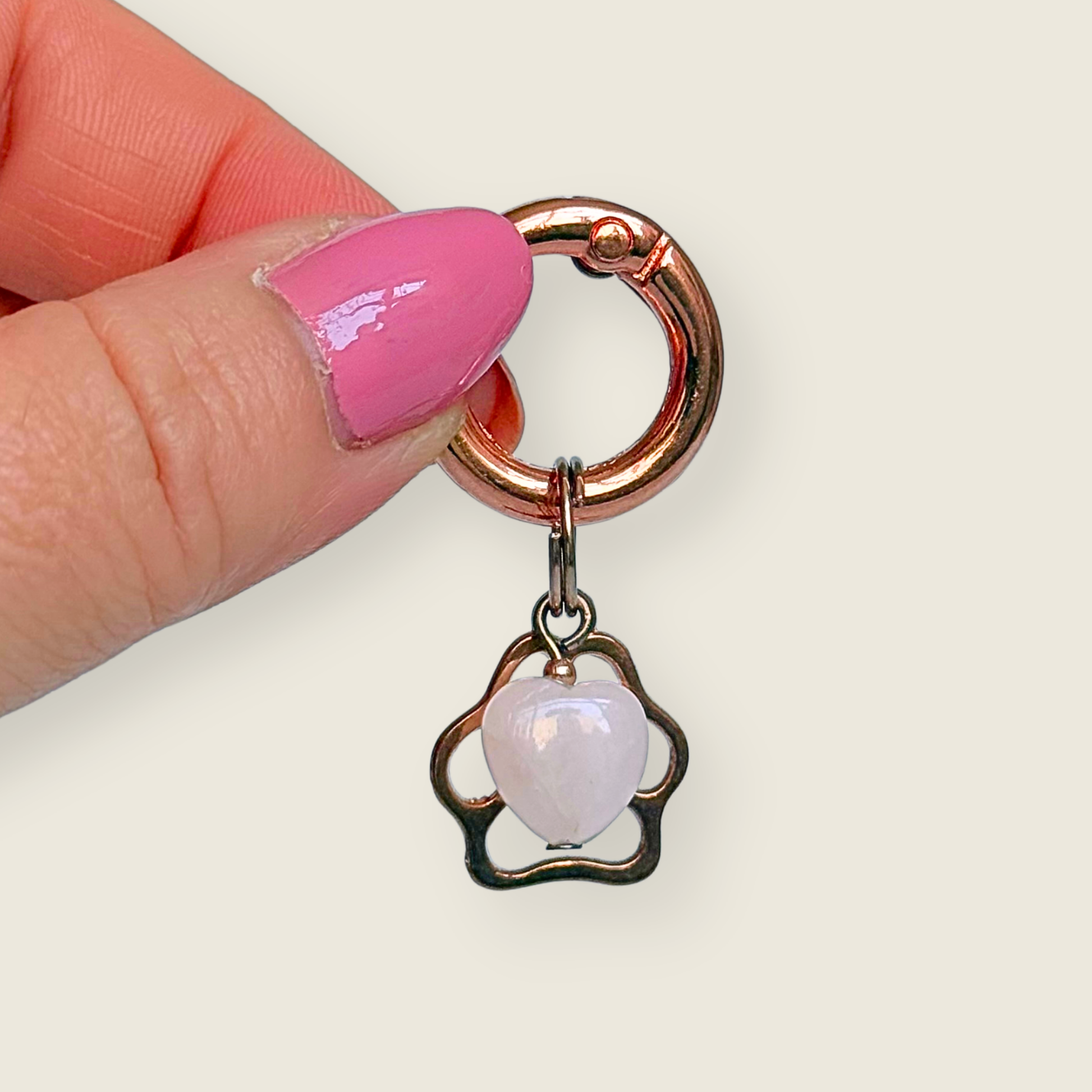 Crystal for dogs pet collar charm featuring a 10mm rose quartz heart shaped bead and a brass rose-gold coloured paw print tag. A stone for love, calm and comfort. Pictured being held against a cream background
