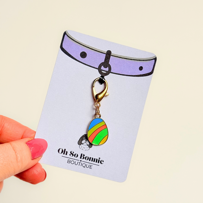 Colourful striped Easter egg enamel dog collar charm that easily attaches to collars and harnesses with a gold plated lobster clasp. Pictured being held on the display card.￼
