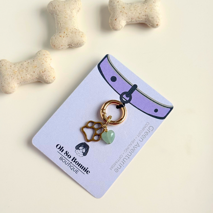 Crystal for dogs pet collar charm featuring a 10mm green aventurine heart shaped bead and a brass gold coloured paw print tag. A stone for comfort, healing and optimism. Pictured on the display card next to some dog bone biscuits.