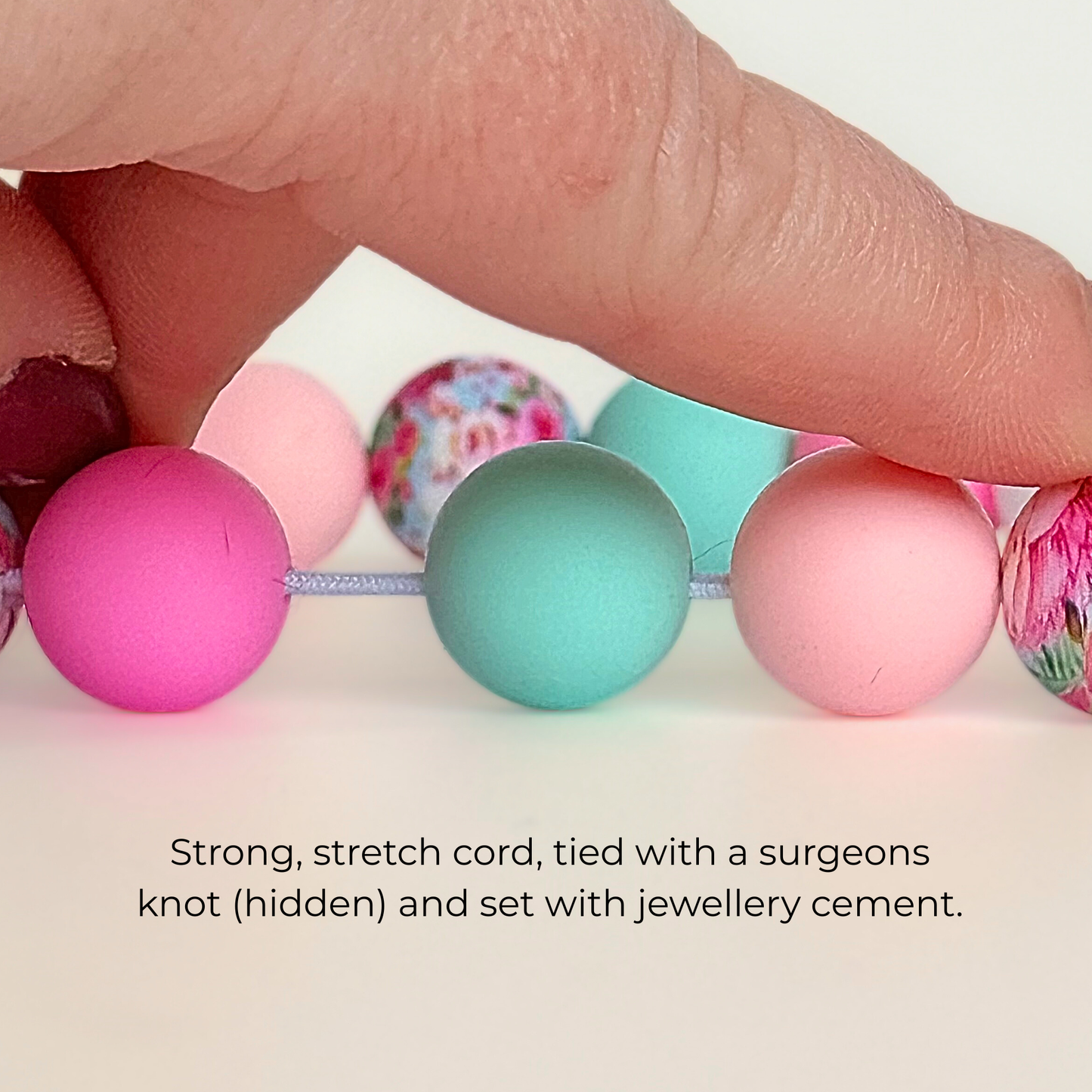 Silicone beaded dog necklace made with 15mm round beads in pink, green, white and a floral flowers print. On a strong, elastic stretch cord. Picture showing the strength of the cord on the beads.￼