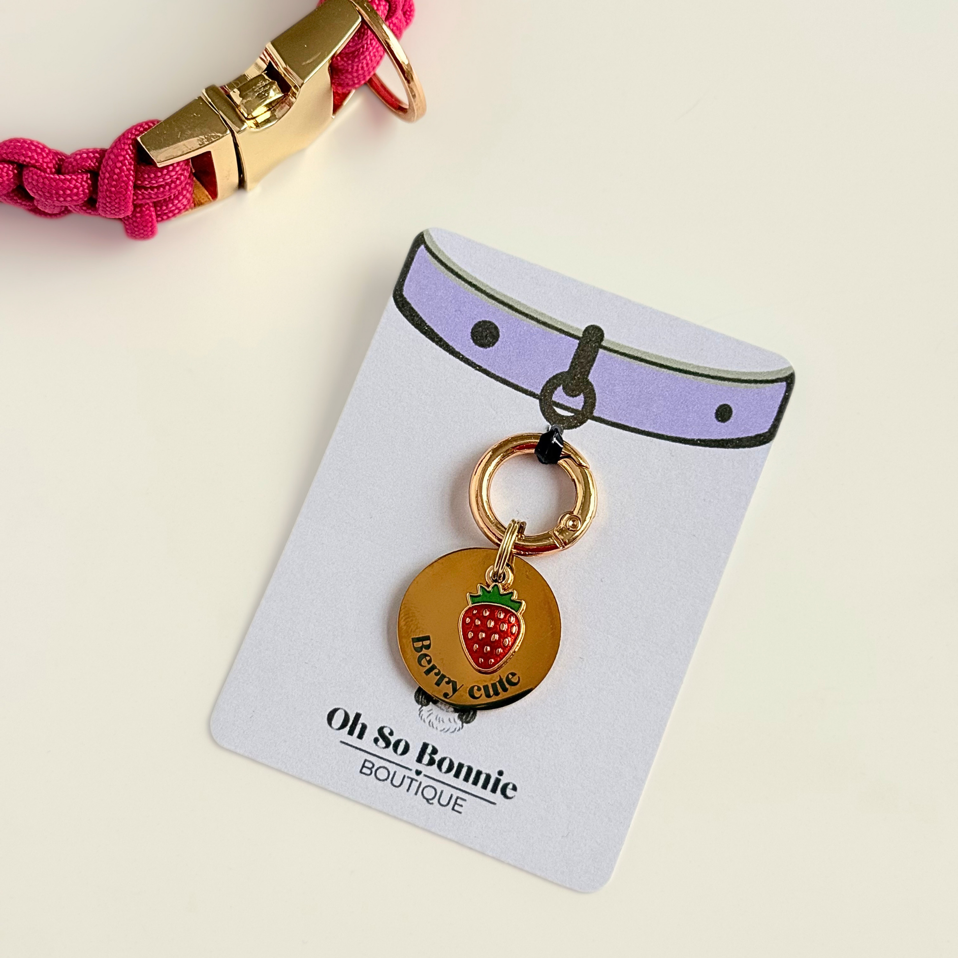 Gold red strawberry dog collar ID tag, Enamel fruit charm with dog name and address details. easily clips onto collar or harness. Next to a dog collar on the display card.