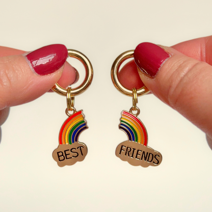 Set of two ‘best friends’ matching dog collar charm and keyring. With enamel rainbow gold plated charms, on secure carabiner style O-rings, for easy use. Pictured both being held against a cream background.