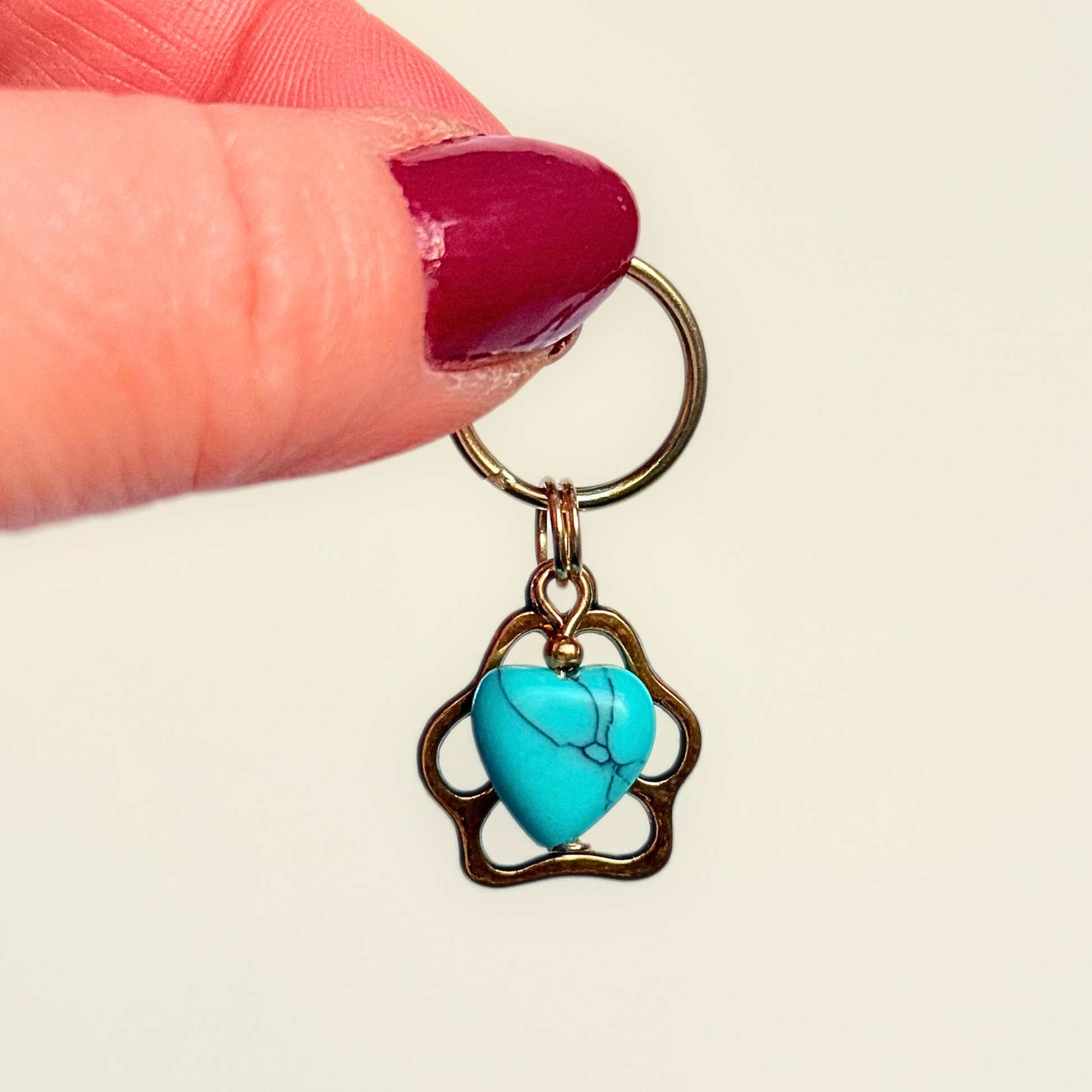 Crystal for dogs pet collar charm featuring a 10mm turquoise blue howlite heart shaped bead and a brass gold coloured paw print tag. Pictured against a cream background.
