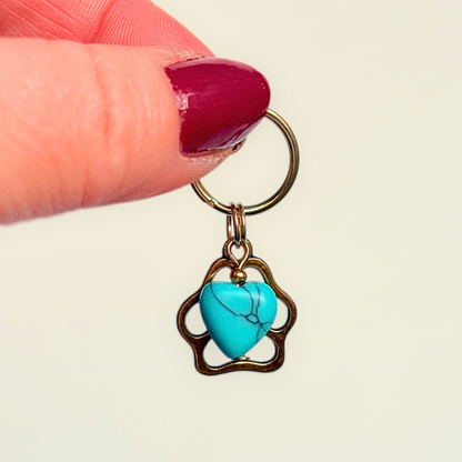 Crystal for dogs pet collar charm featuring a 10mm turquoise blue howlite heart shaped bead and a brass gold coloured paw print tag. Pictured against a cream background.