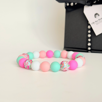 Silicone beaded dog necklace made with 15mm round beads in pink, green, white and a floral flowers print. On a strong, elastic stretch cord. Pictured in front of the gift box.￼