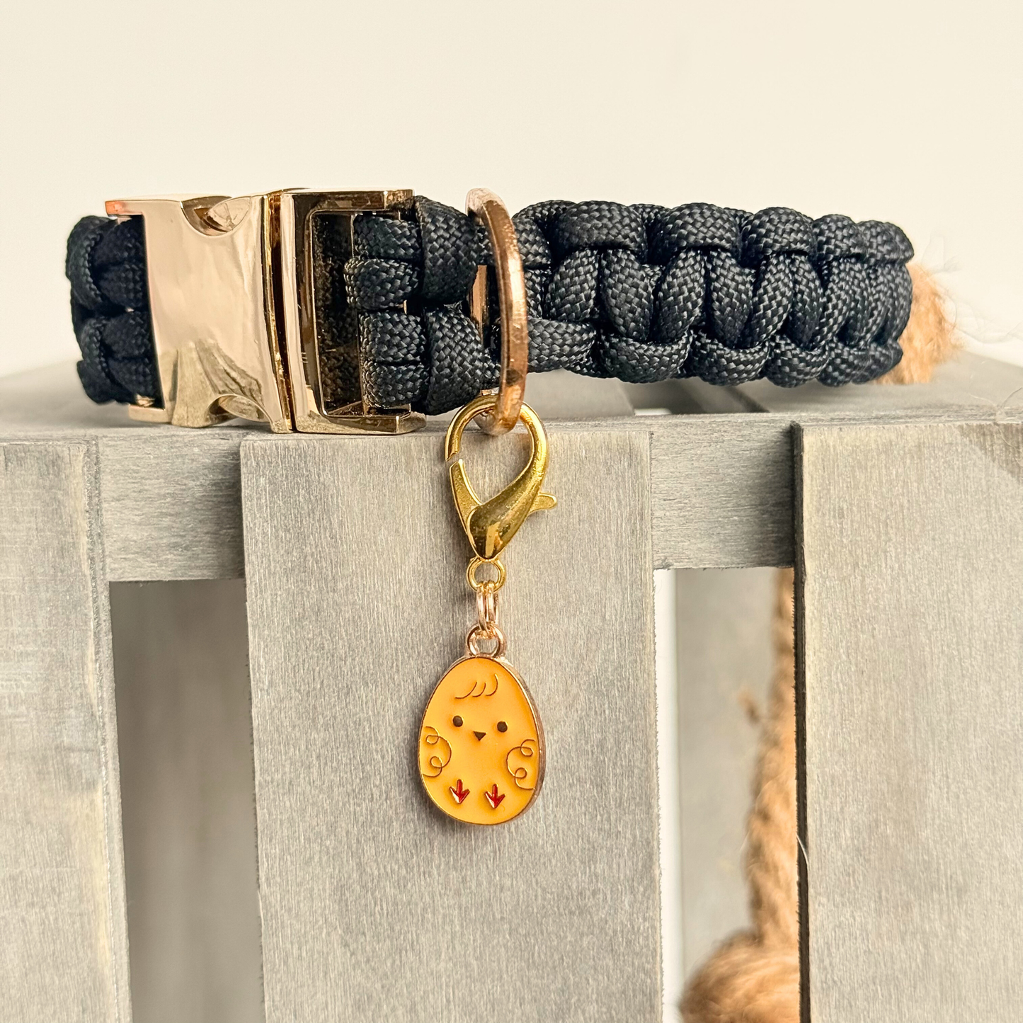 Yellow chick Easter egg enamel dog collar charm that easily attaches to collars and harnesses with a gold plated lobster clasp. Pictured close up, attached to a black paracord dog collar.