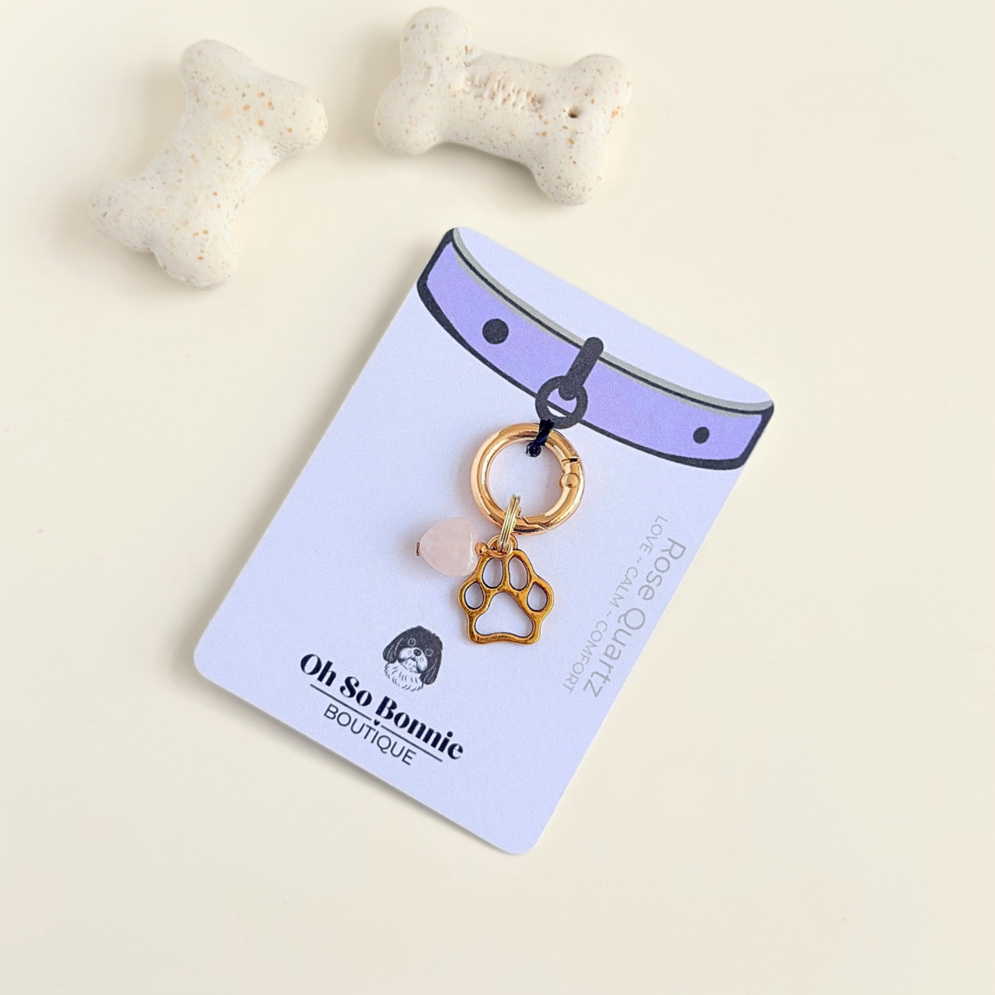 Crystal for dogs pet collar charm featuring a 10mm rose quartz heart shaped bead and a brass gold coloured paw print tag. A stone for love, calm and comfort. Pictured on the display card, next to some dog bone biscuits