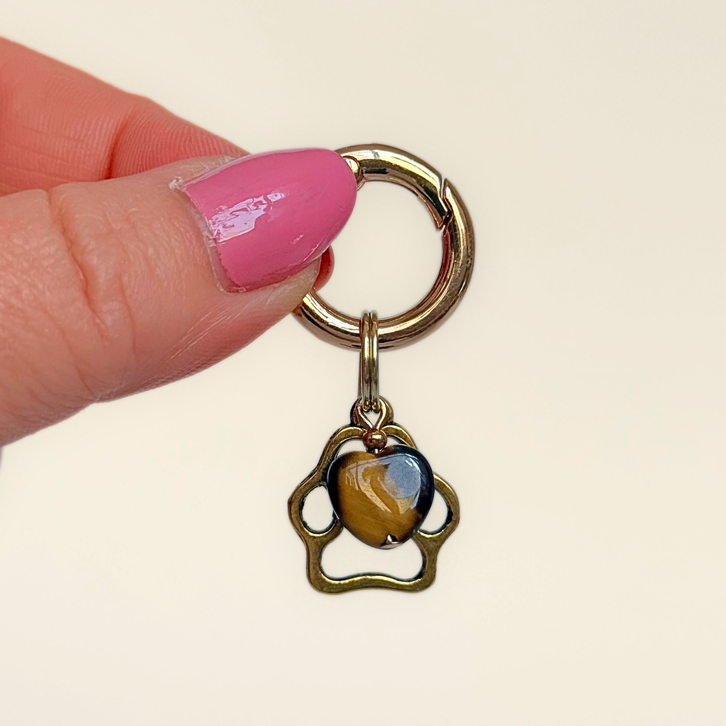Crystal for dogs pet collar charm featuring a 10mm tigers eye heart shaped bead and a brass gold coloured paw print tag. Pictured being held up.