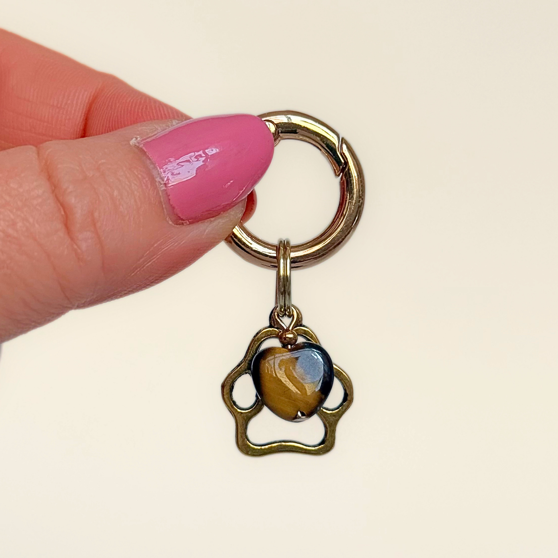 Crystal for dogs pet collar charm featuring a 10mm tigers eye heart shaped bead and a brass gold coloured paw print tag. Pictured being held up.