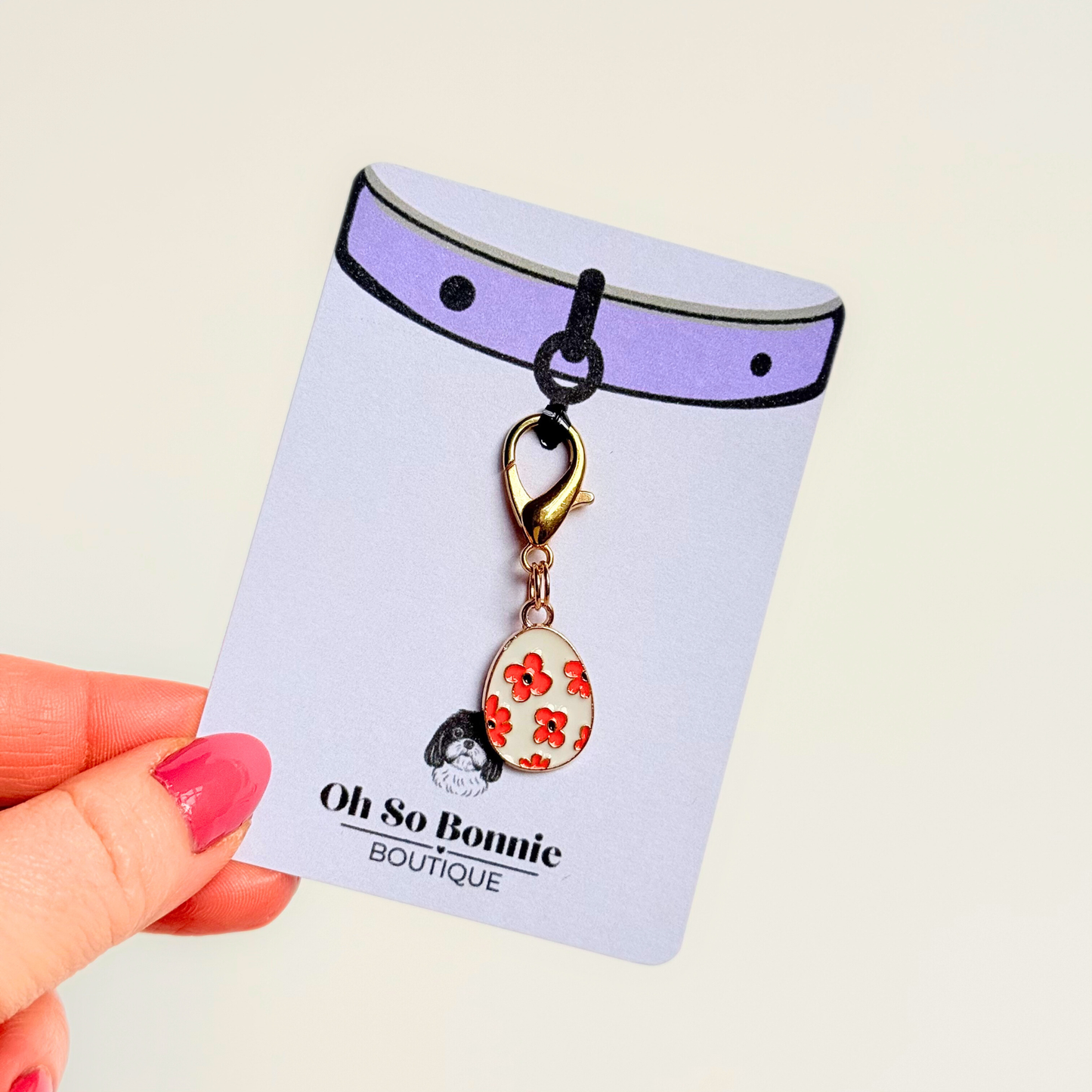 White with red flowers Easter egg enamel dog collar charm that easily attaches to collars and harnesses with a gold plated lobster clasp. Pictured on the display card.￼