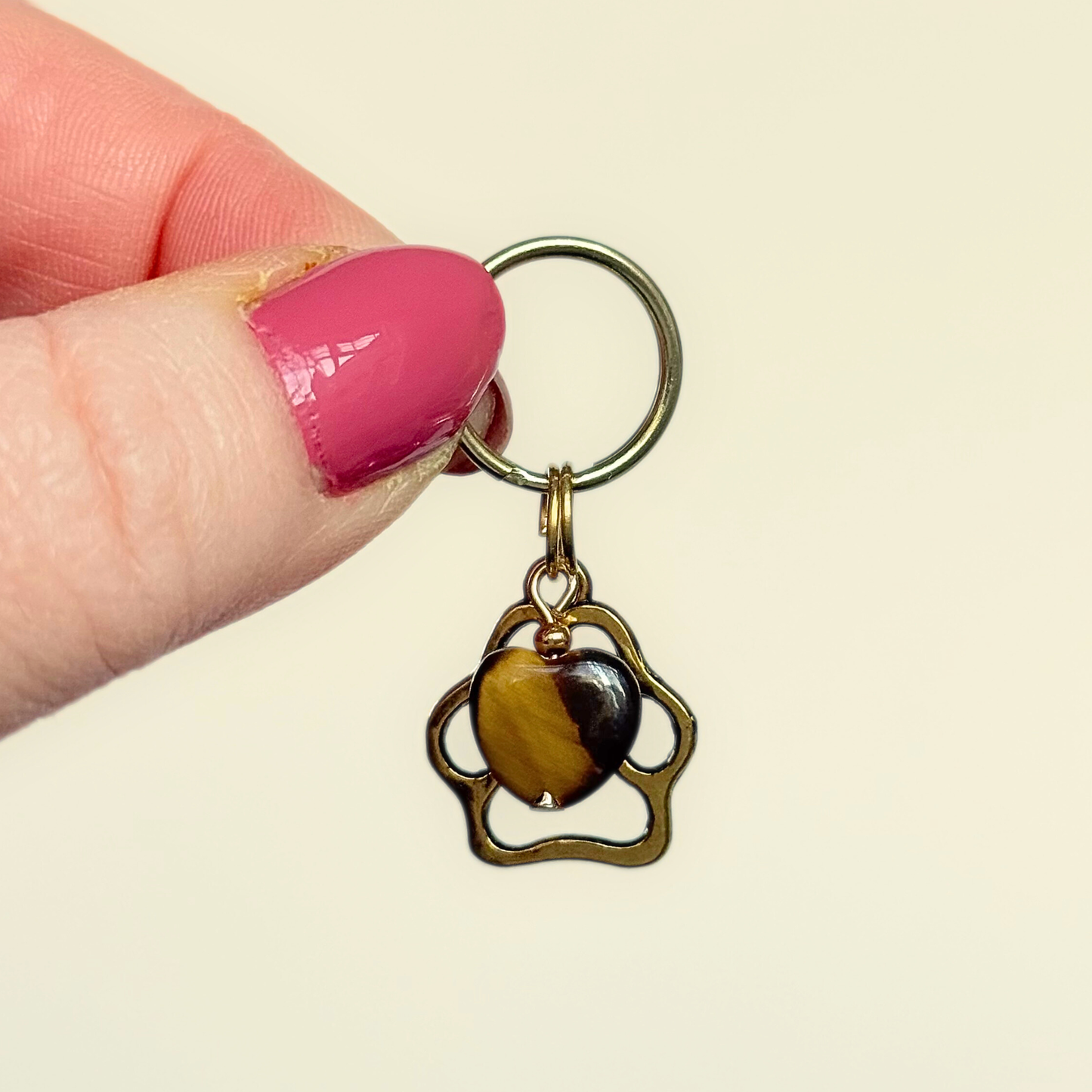 Crystal for dogs pet collar charm featuring a 10mm tigers eye heart shaped bead and a brass gold coloured paw print tag. Pictured being held up.