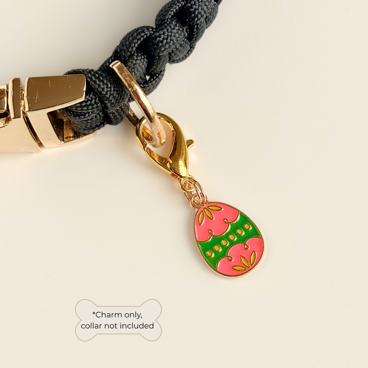 Colourful pink and green patterned Easter egg enamel dog collar charm that easily attaches to collars and harnesses with a gold plated lobster clasp. Pictured attached to a black paracord dog collar.￼