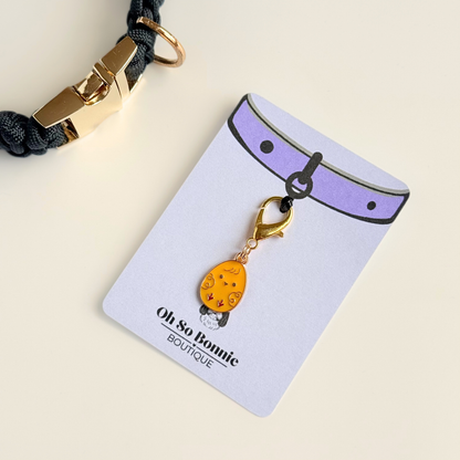 Yellow chick Easter egg enamel dog collar charm that easily attaches to collars and harnesses with a gold plated lobster clasp. Pictured on the display card next to a black paracord dog collar.￼