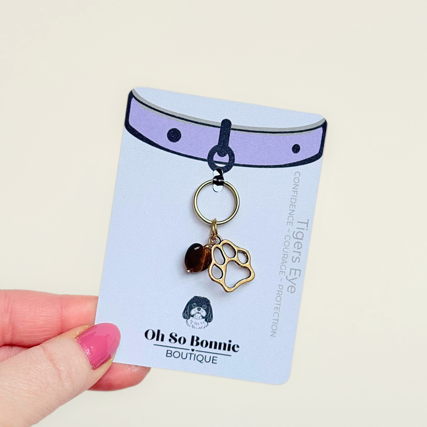 Crystal for dogs pet collar charm featuring a 10mm tigers eye heart shaped bead and a brass gold coloured paw print tag. Pictured on the display card.