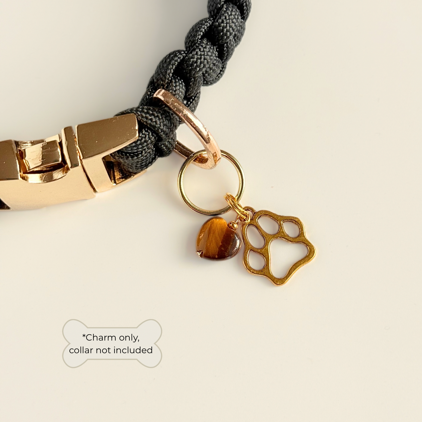 Crystal for dogs pet collar charm featuring a 10mm tigers eye heart shaped bead and a brass gold coloured paw print tag. Pictured attached to a black paracord dog collar.