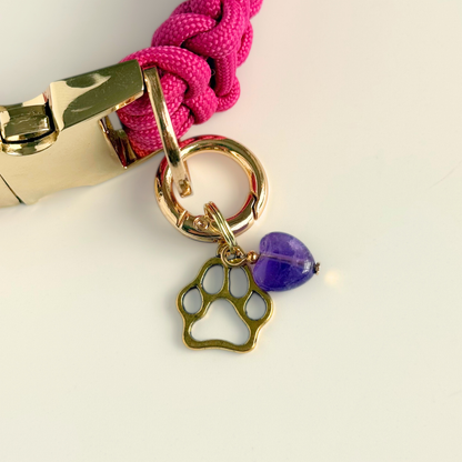 Crystal for dogs pet collar charm featuring a 10mm purple amethyst heart shaped bead and a brass gold coloured paw print tag. Pictured attached to a pink paracord collar.