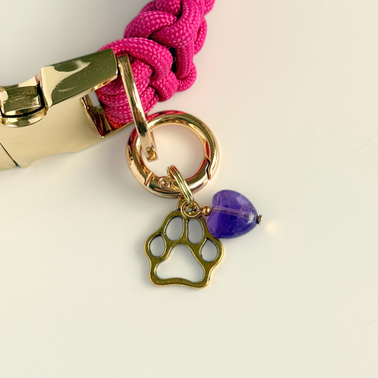 Crystal for dogs pet collar charm featuring a 10mm purple amethyst heart shaped bead and a brass gold coloured paw print tag. Pictured attached to a pink paracord collar.