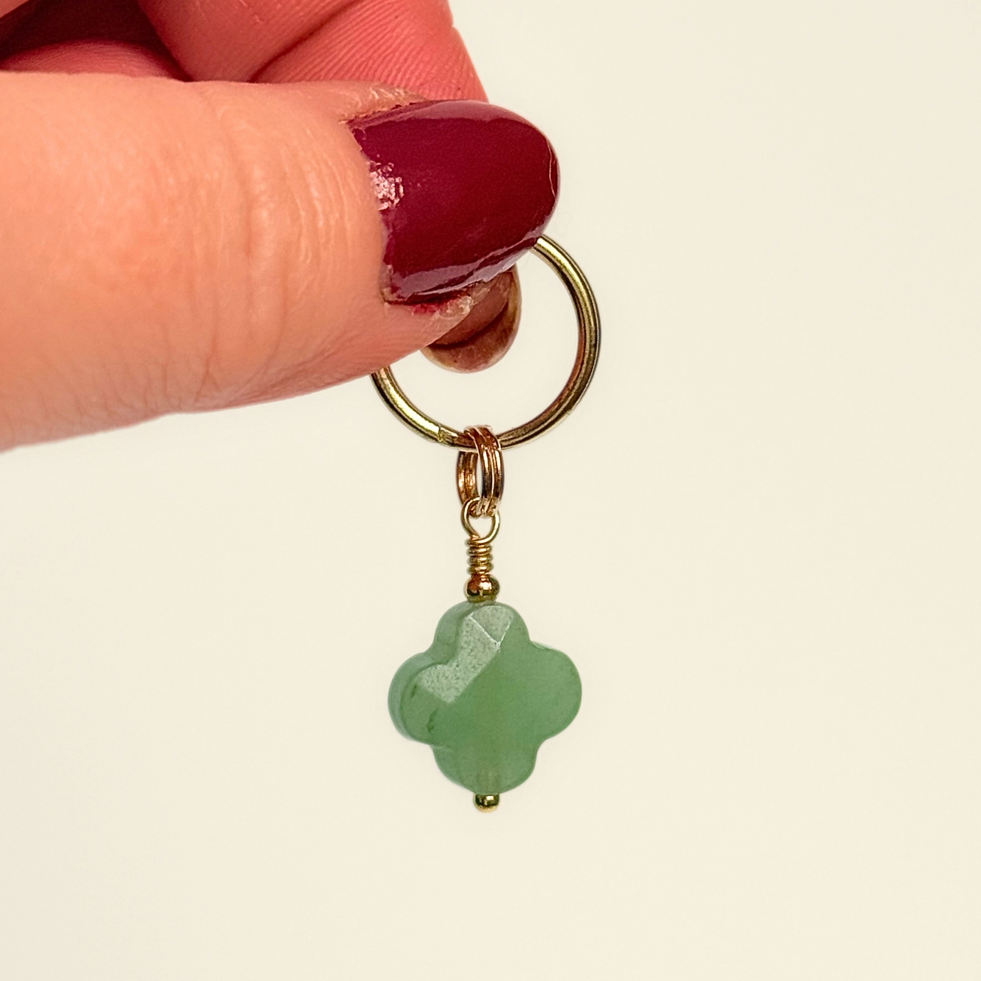 Green aventurine four leaf clover shaped crystal dog collar charm. Crystals for dogs, gemstone for optimism, healing and comfort. Pictured held against a cream background.