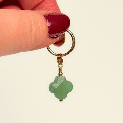 Green aventurine four leaf clover shaped crystal dog collar charm. Crystals for dogs, gemstone for optimism, healing and comfort. Pictured held against a cream background.