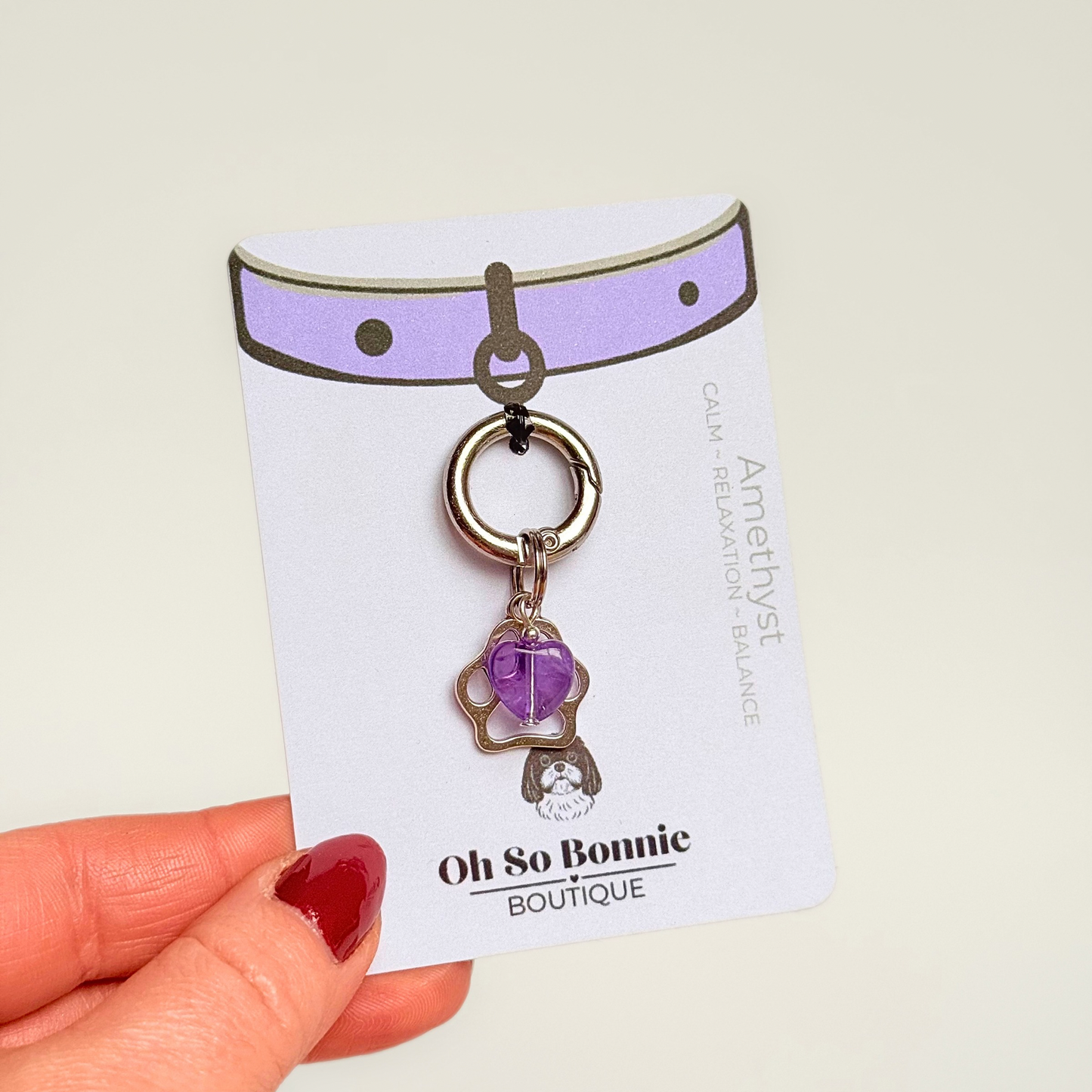 Crystal for dogs pet collar charm featuring a 10mm purple amethyst heart shaped bead and a brass silver coloured paw print tag. Pictured on the display card.