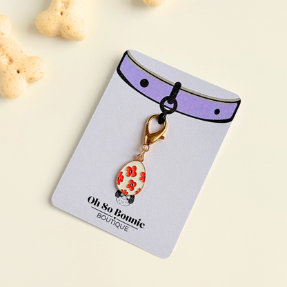 White with red flowers Easter egg enamel dog collar charm that easily attaches to collars and harnesses with a gold plated lobster clasp. Pictured on the display card next to some dog bone biscuits.￼