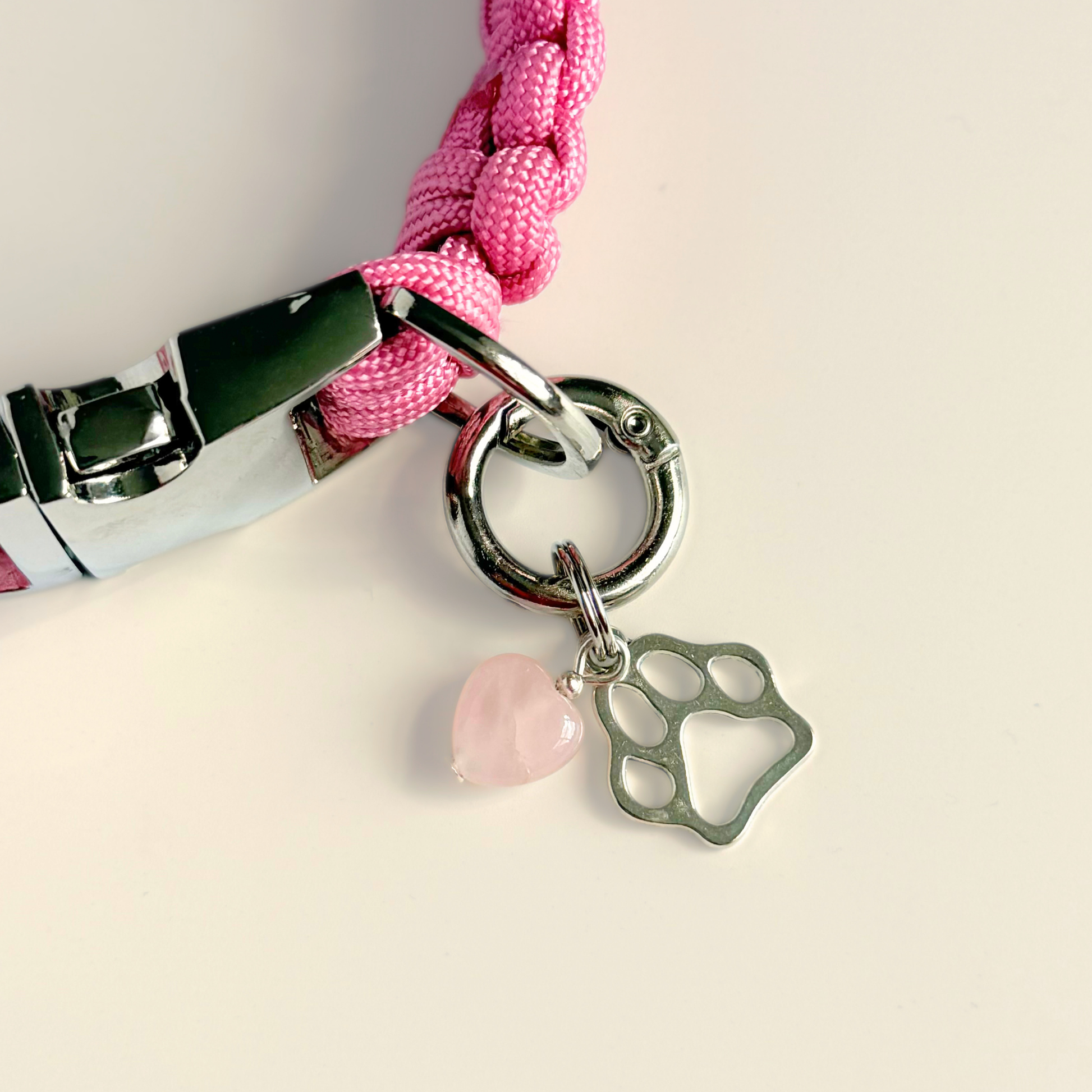Crystal for dogs pet collar charm featuring a 10mm rose quartz heart shaped bead and a brass silver coloured paw print tag. A stone for love, calm and comfort. Pictured attached to a pink paracord dog collar against a cream background.