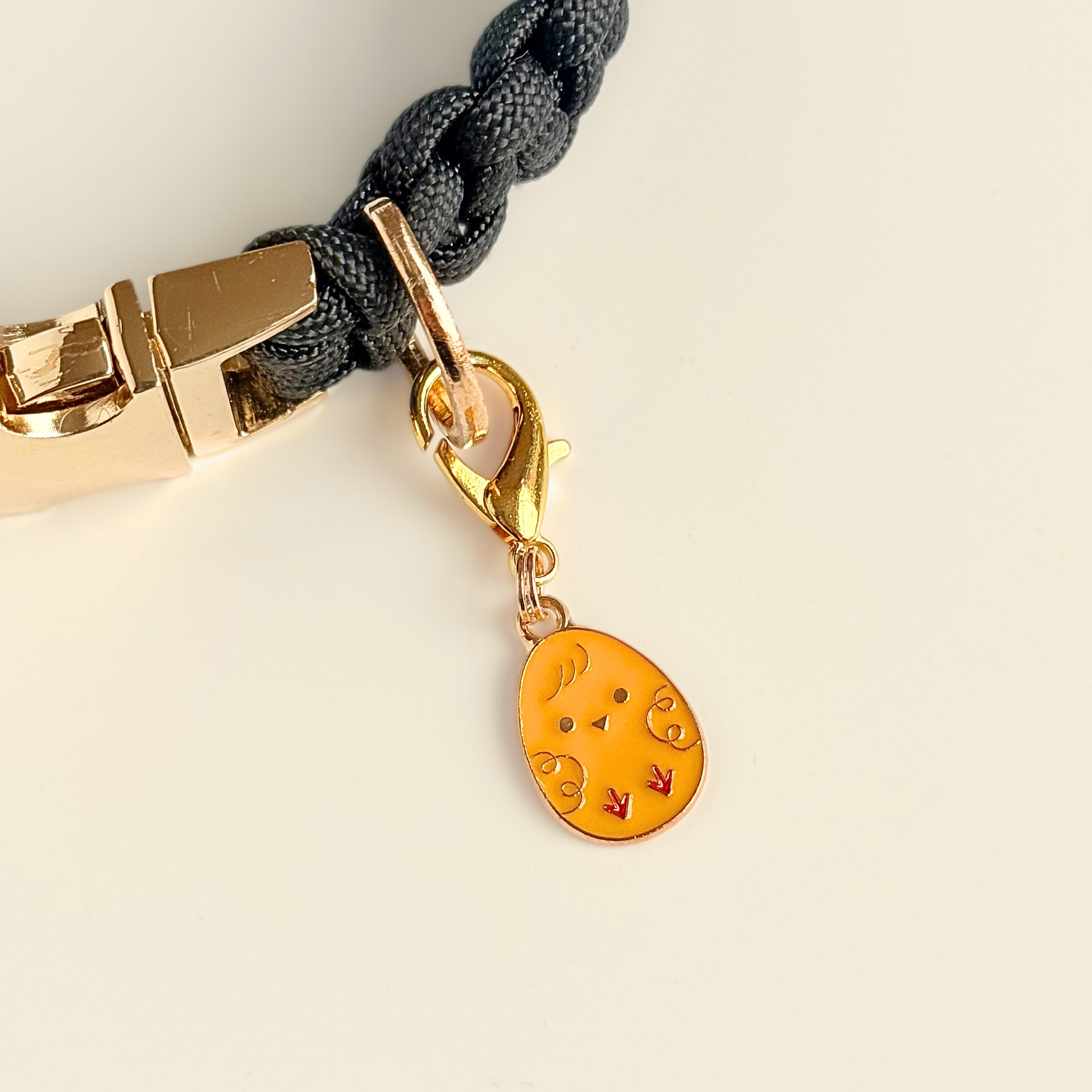 Yellow chick Easter egg enamel dog collar charm that easily attaches to collars and harnesses with a gold plated lobster clasp. Pictures attached to a black paracord dog collar.