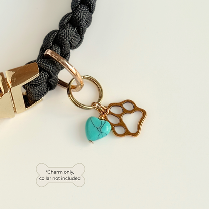 Crystal for dogs pet collar charm featuring a 10mm turquoise blue howlite heart shaped bead and a brass gold coloured paw print tag. Pictured attached to a black paracord dog collar. 