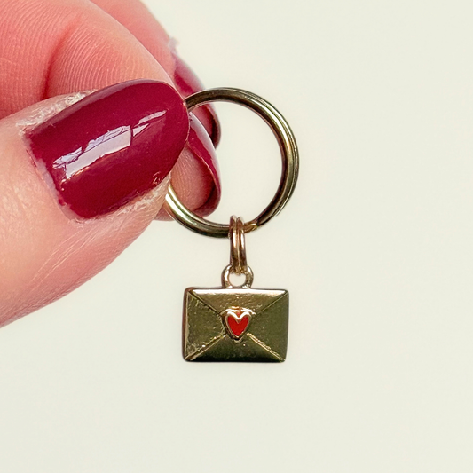 Gold plated brass envelope dog collar charm featuring a red enamel heart. Pictured being held up.