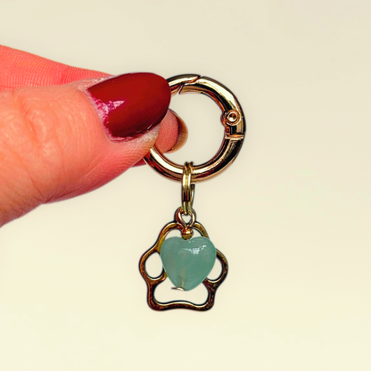 Crystal for dogs pet collar charm featuring a 10mm green aventurine heart shaped bead and a brass gold coloured paw print tag. A stone for comfort, healing and optimism. Pictured being held against a cream background.