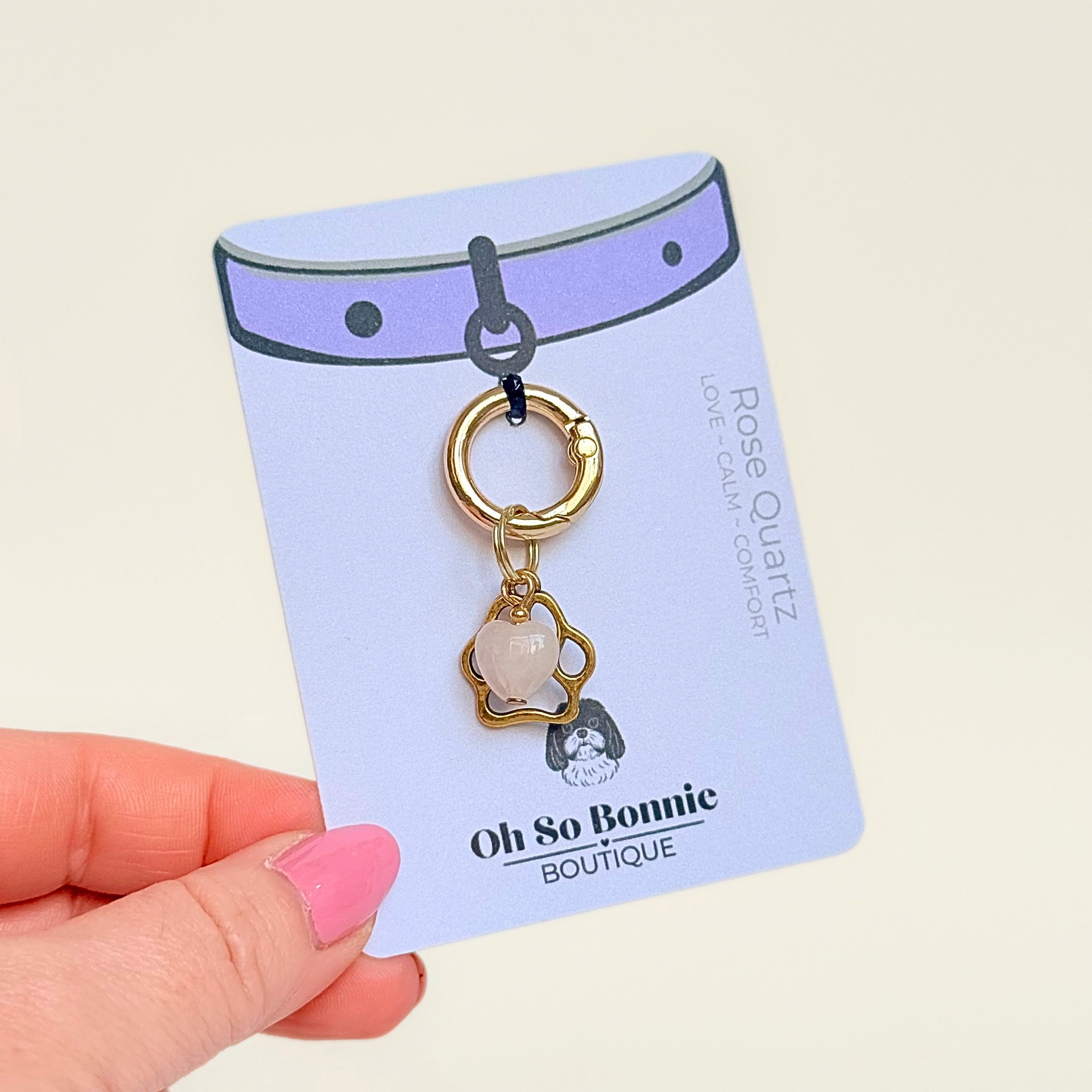 Crystal for dogs pet collar charm featuring a 10mm rose quartz heart shaped bead and a brass gold coloured paw print tag. A stone for love, calm and comfort. Pictured on the display card.