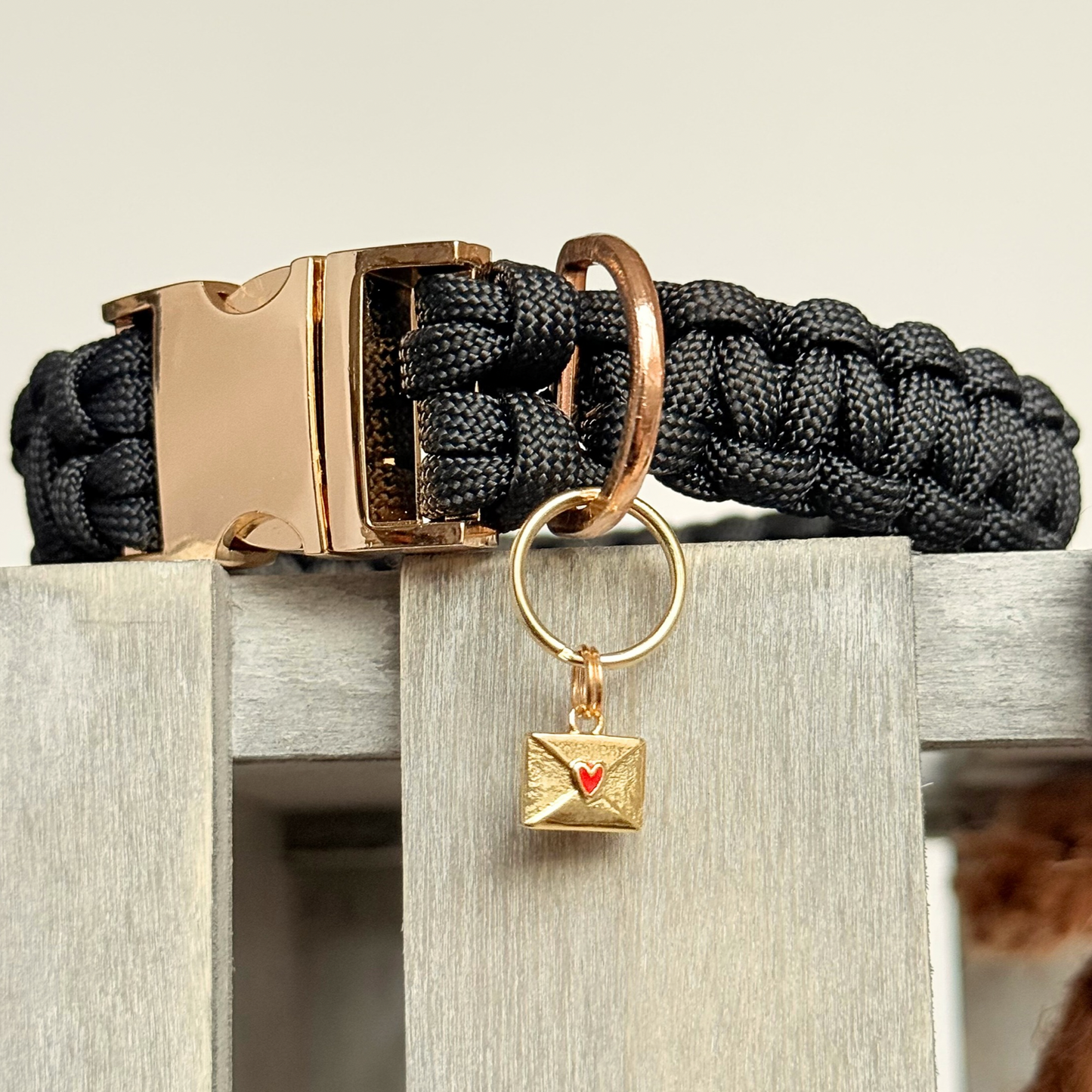 Gold plated brass envelope dog collar charm featuring a red enamel heart. Close-up picture of the charm attached to a black paracord dog collar.￼