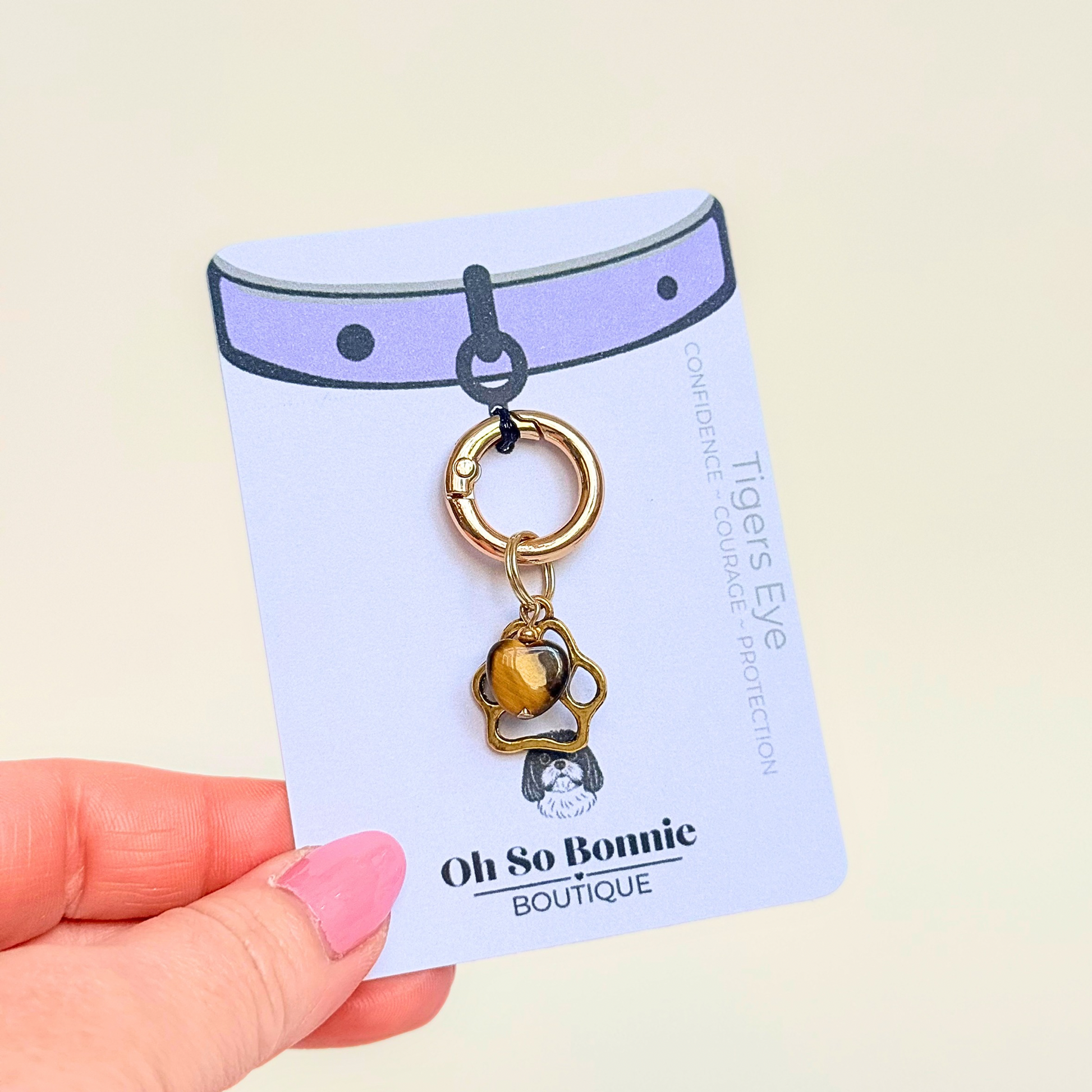 Crystal for dogs pet collar charm featuring a 10mm tigers eye heart shaped bead and a brass gold coloured paw print tag. Pictured on the display card.