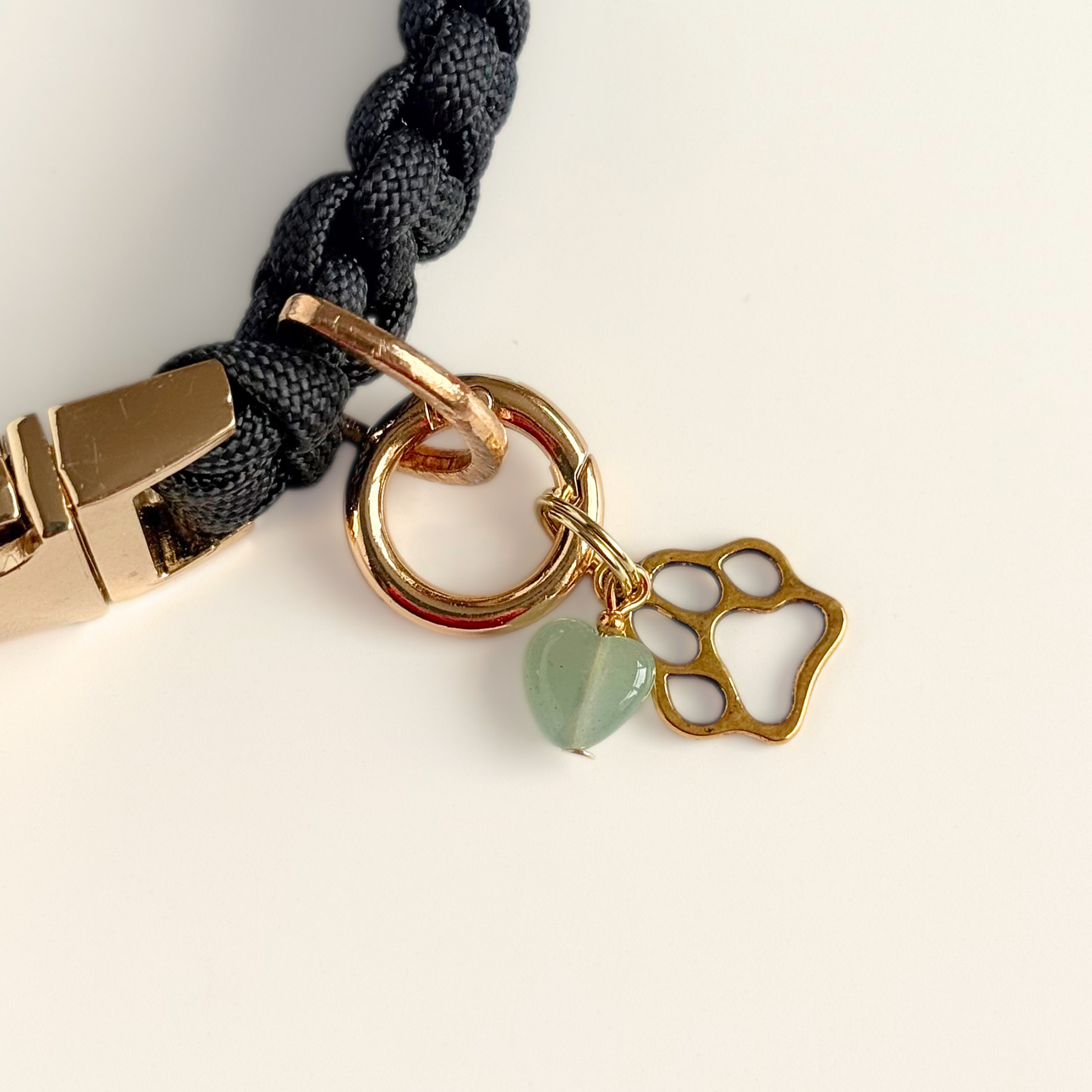 Crystal for dogs pet collar charm featuring a 10mm green aventurine heart shaped bead and a brass gold coloured paw print tag. A stone for comfort, healing and optimism. Pictured attached to a black paracord dog collar against a cream background.