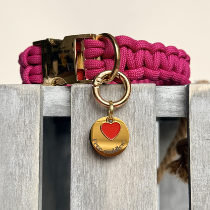 Gold plated brass and stainless steel 20mm dog collar charm with ID tag. Personalised custom identification tag with a small, red love heart charm, on a  brass carabiner style o-ring. Engraved with the words ‘Free cuddles’! on the front. Pictured attached to a pink paracord dog collar.