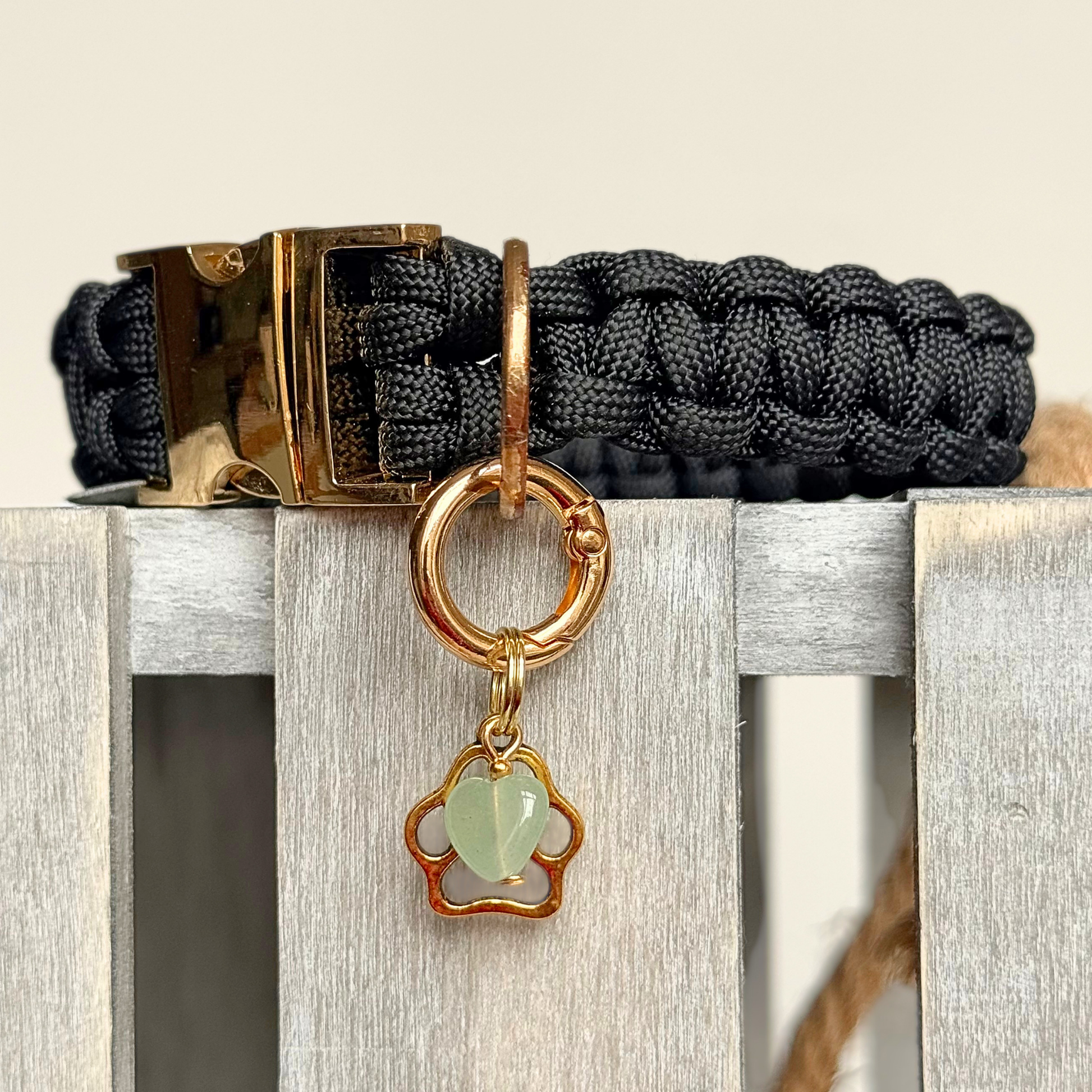 Crystal for dogs pet collar charm featuring a 10mm green aventurine heart shaped bead and a brass gold coloured paw print tag. A stone for comfort, healing and optimism. Pictured attached to a black paracord dog collar.