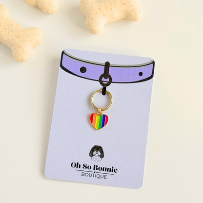 Rainbow striped heart shaped dog collar charm made with an enamel charm and a gold plated brass split ring. Pictured on the display card, next to some dog biscuits.