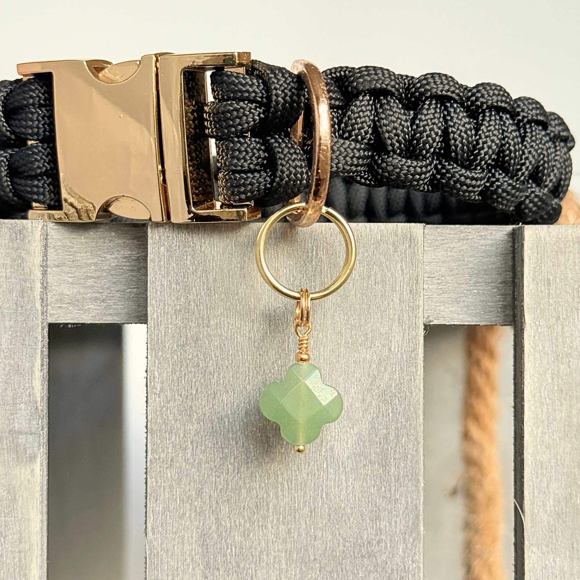 Green aventurine four leaf clover shaped crystal dog collar charm. Crystals for dogs, gemstone for optimism, healing and comfort. Close up picture attached to a black paracord dog collar.