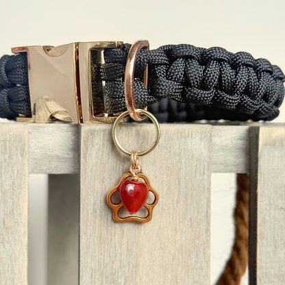 Crystal for dogs pet collar charm featuring a 10mm red carnelian heart shaped bead and a brass gold coloured paw print tag. A stone for confidence, vitality and motivation. Close up pictured attached to a black paracord dog collar.