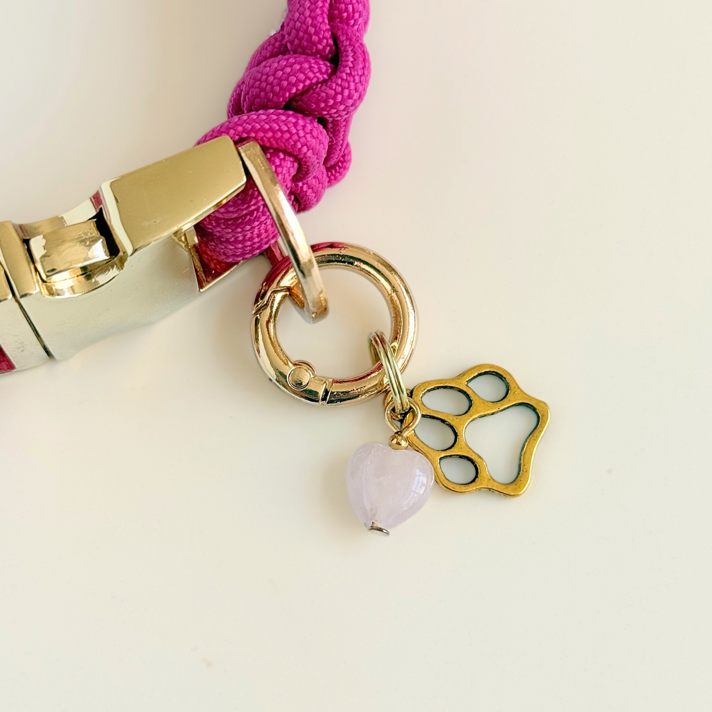 Crystal for dogs pet collar charm featuring a 10mm rose quartz heart shaped bead and a brass gold coloured paw print tag. A stone for love, calm and comfort. Pictured attached to a pink paracord dog collar against a cream background.
