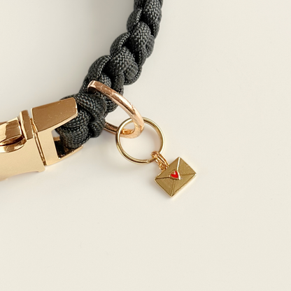 Gold plated brass envelope dog collar charm featuring a red enamel heart. Pictured attached to a black paracord dog collar.￼