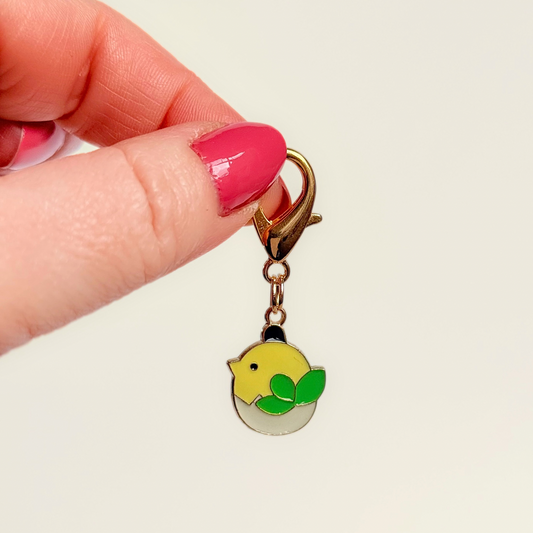Enamel and gold plated hatching yellow chick dog collar charm. Easy to clip onto collars with a lobster clasp. Pictured being held against a cream background.￼