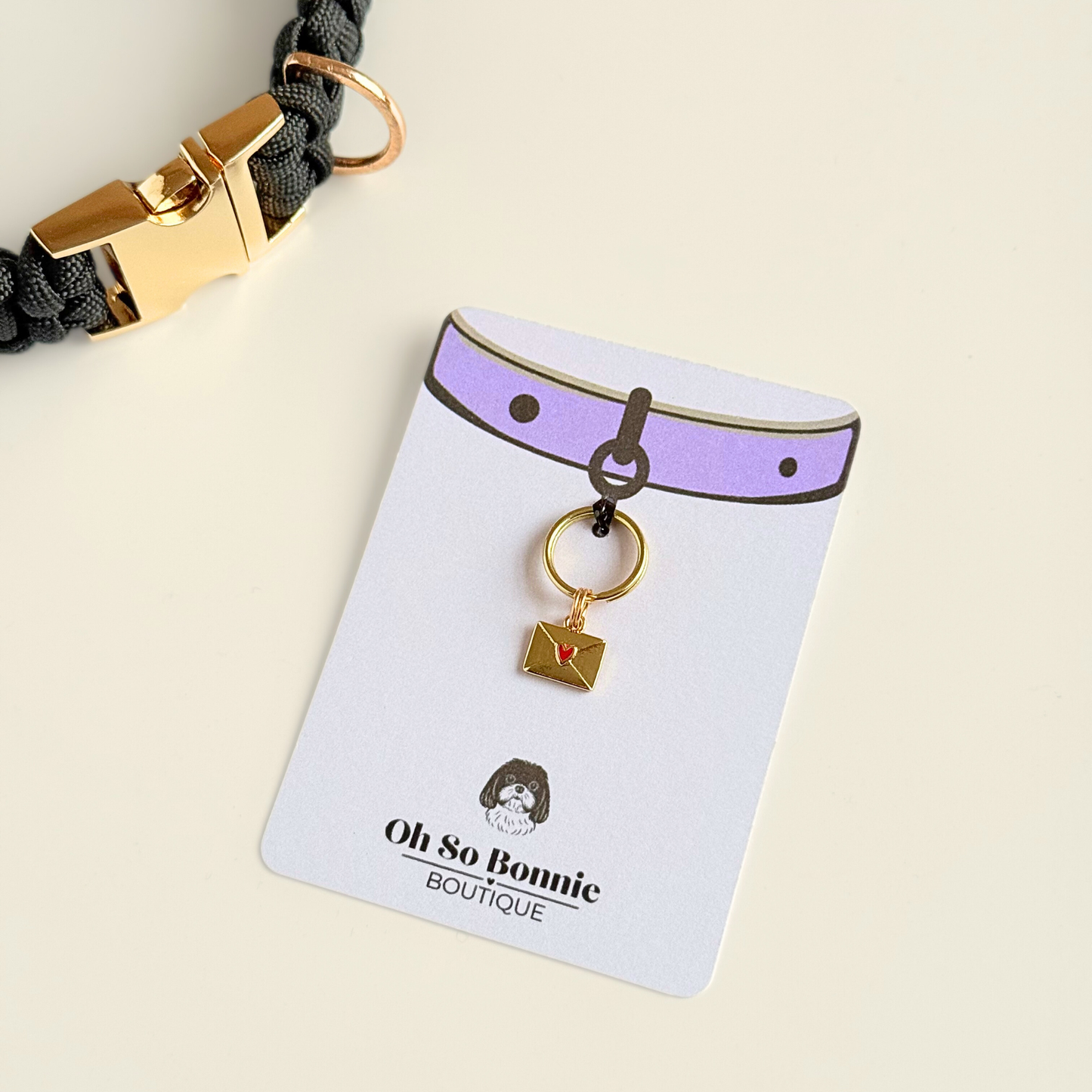 Gold plated brass envelope dog collar charm featuring a red enamel heart. Pictured on the display card next to a black paracord dog collar.￼