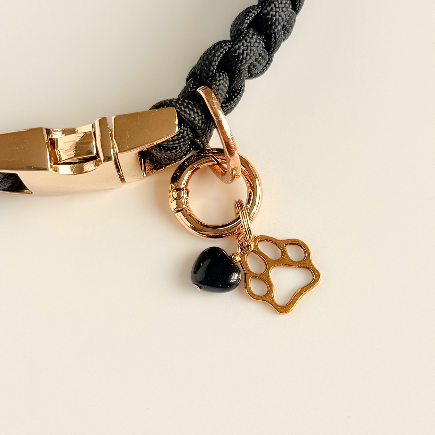 Crystal for dogs pet collar charm featuring a 10mm black onyx heart shaped bead and a brass gold coloured paw print tag. A stone for protection, strength and stability. Pictured clipped on to a black paracord dog collar
