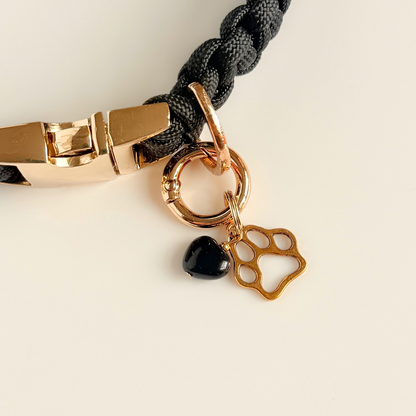 Crystal for dogs pet collar charm featuring a 10mm black onyx heart shaped bead and a brass gold coloured paw print tag. A stone for protection, strength and stability. Pictured clipped on to a black paracord dog collar