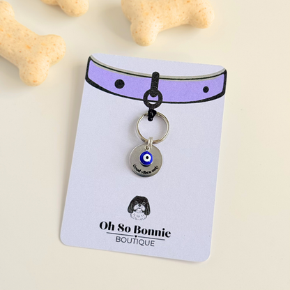 Silver plated brass and stainless steel 15mm dog collar charm with ID tag. Personalised custom identification tag with a small, blue Turkish Evil Eye charm, on a 15mm silver split ring. Engraved with the words ‘Good vibes only’ on the front. Pictured against a cream background on the display card.